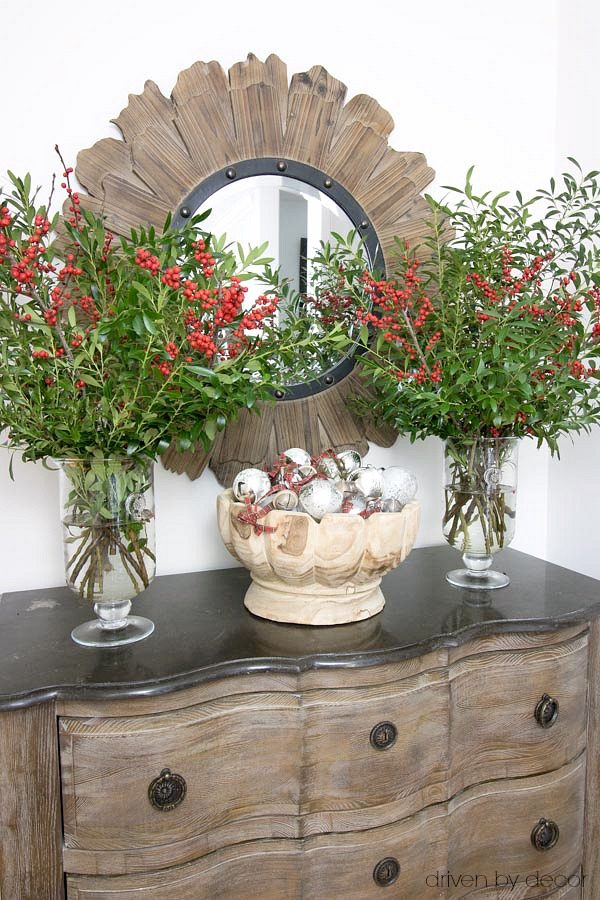 Christmas home tour - a bowl full of ornaments flanked by vases of boxwood branches and berries for entryway Christmas decor