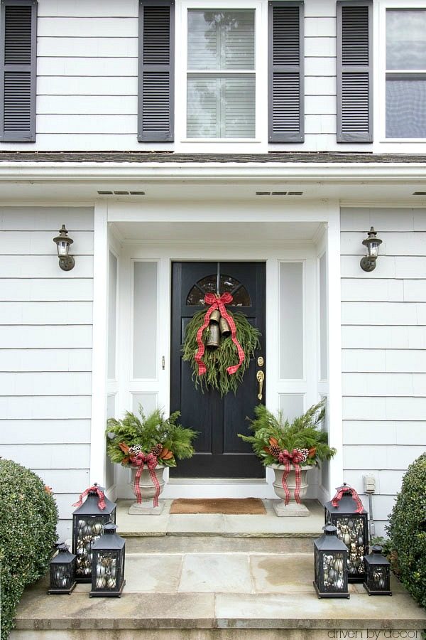 Christmas house tour - a trio of lanterns filled with ornaments, planters filled with greenery, and a greenery swag on the front door are simple porch decorations for Christmas
