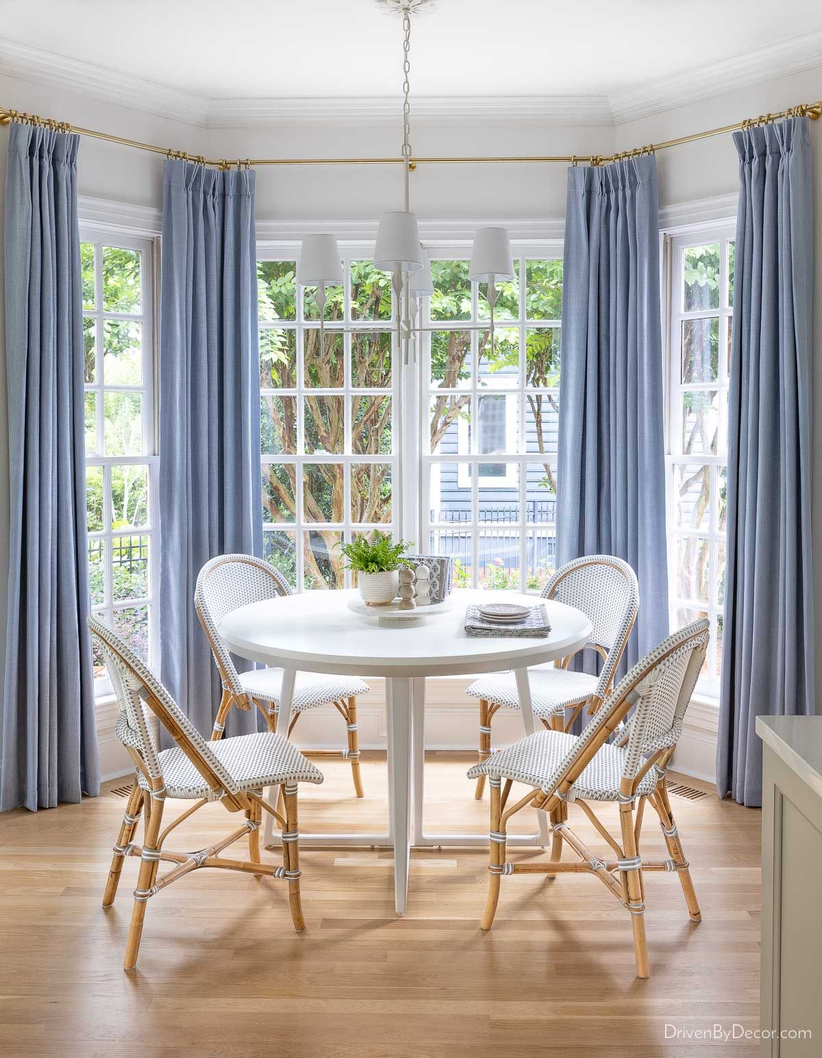Bay window breakfast nook with light blue curtains and matte white chandelier