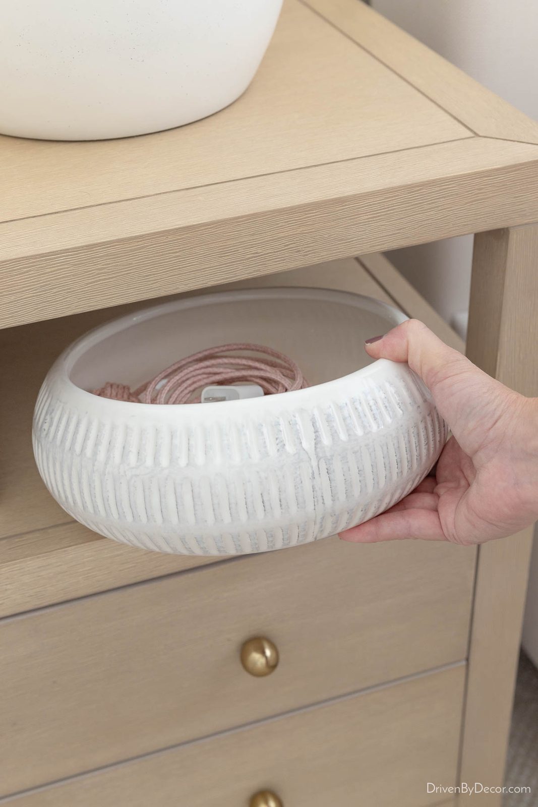 Shallow white planter used as bowl to hold charging cable on nightstand