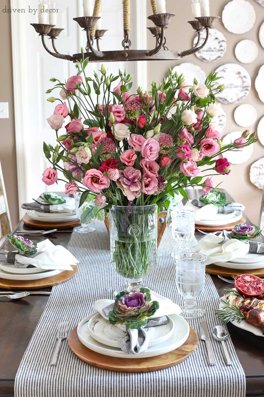 Simple dining room table setting for Thanksgiving with fresh flowers for a centerpiece and faux kale tucked into napkins