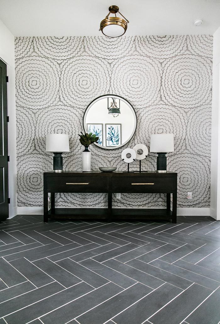 Stunning entry designed by Sita Montgomery Interiors with black herringbone floors and a long console with twin lamps and a round mirror.