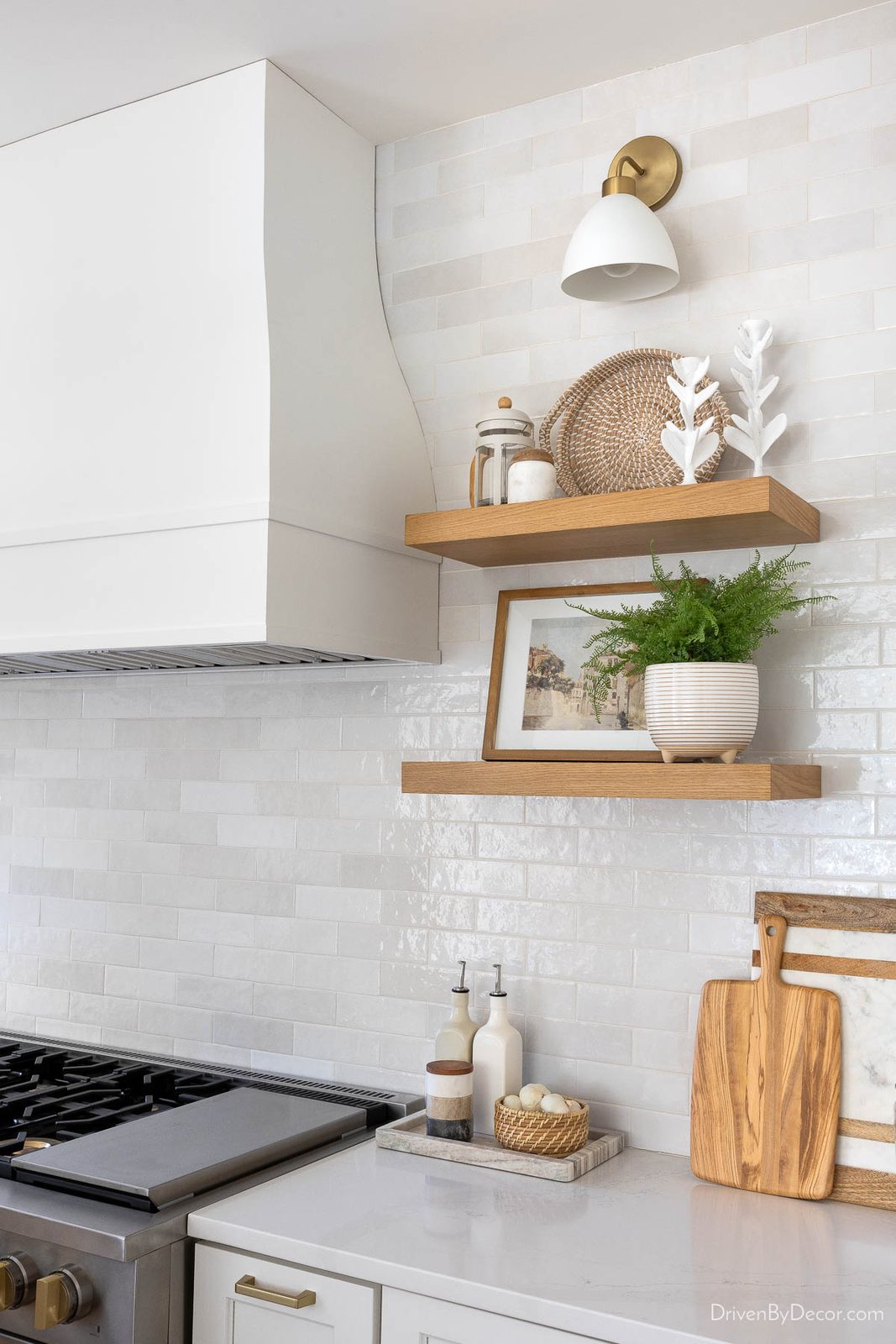 Brass and matte white sconce over floating wood shelves in kitchen