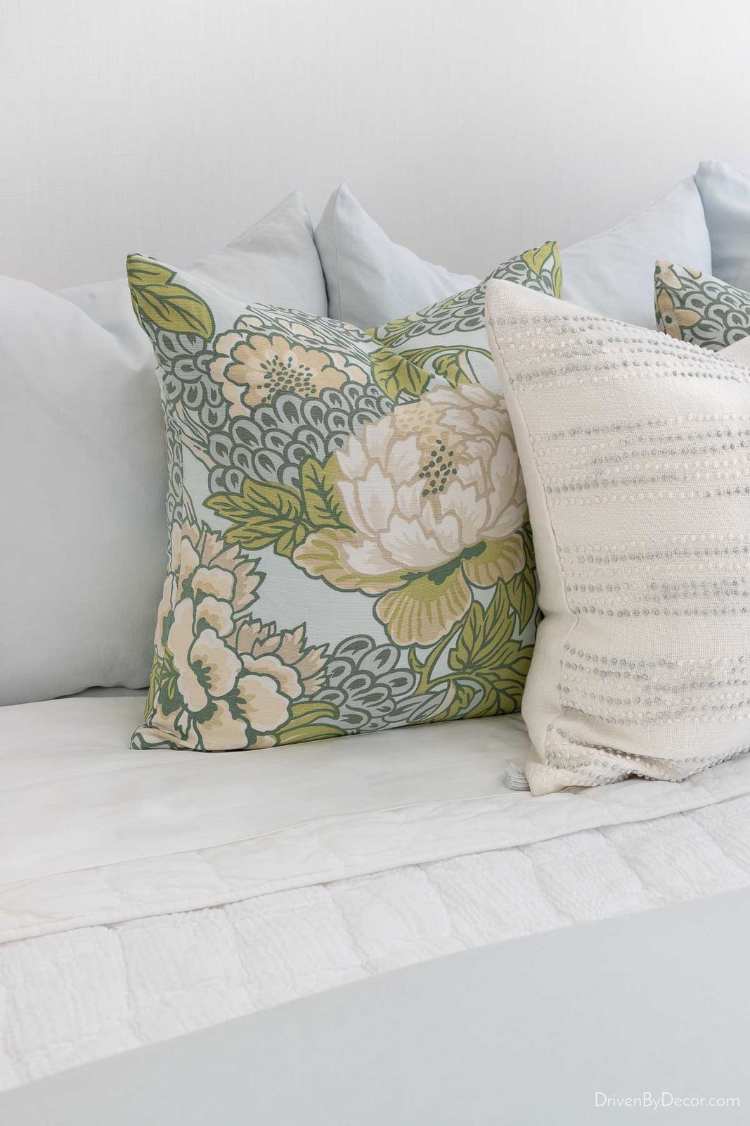 Light blue Euro shams, patterned pillows, and white textured pillows on bed