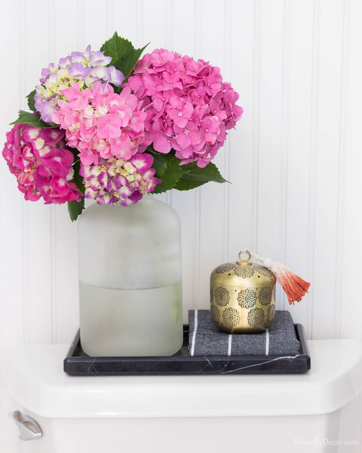 Black marble tray on toilet tank with vase of flowers and candle