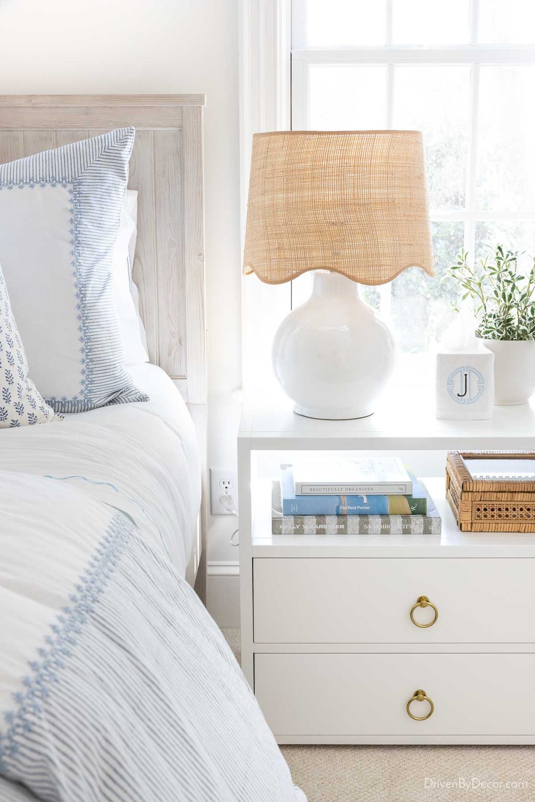 Round white lamp with scalloped rattan shade on bedroom nightstand