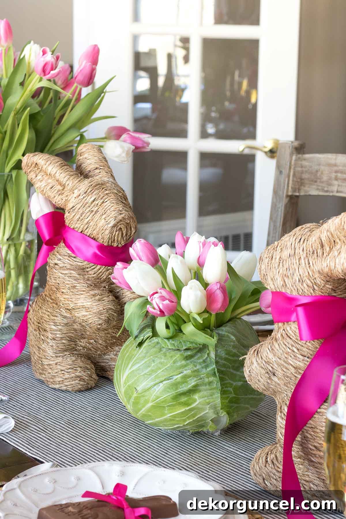 Charming Easter table centerpiece featuring two twine Easter bunnies flanking a vibrant green cabbage, artfully hollowed out and filled with fresh tulips.