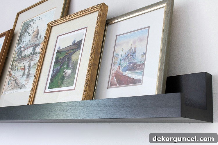 Above TV Shelf: Smart Storage, Seamless Style 8 Side view of a black ledge shelf holding framed art prints, demonstrating how the prints are securely nestled within the shelf's front lip, preventing them from falling.