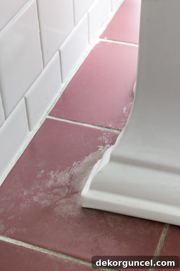 How to Paint a Tile Floor: Essential Tools and Proven Tips 4 Close-up of severely stained and corroded ceramic tile floor behind a pedestal sink, highlighting the damage before painting.