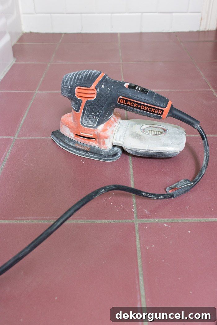 How to Paint a Tile Floor: Essential Tools and Proven Tips 7 Detail shot of a handheld electric sander being used to prepare ceramic tile floors, emphasizing the importance of scuffing the surface for paint adhesion.