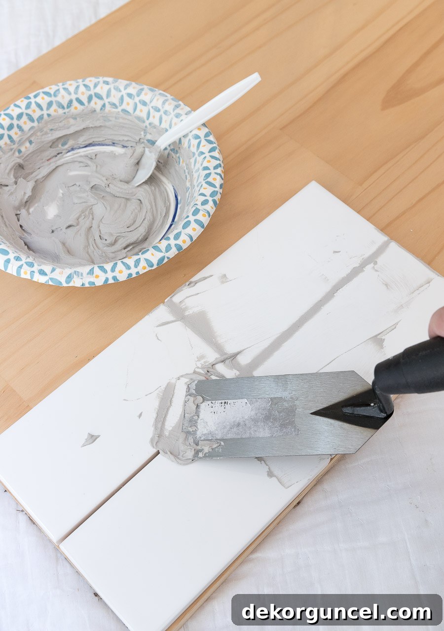White Subway Tile and Gray Grout My Favorite Shades 6 Applying gray grout to white subway tile sample board with a trowel, a crucial step for choosing the best grout color.
