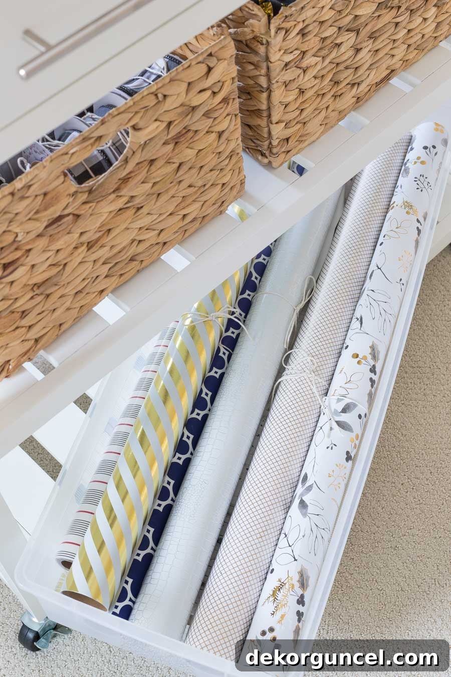 A perfectly sized clear storage bin on the bottom shelf of the gift wrapping station, neatly holding rolls of gift wrapping paper.