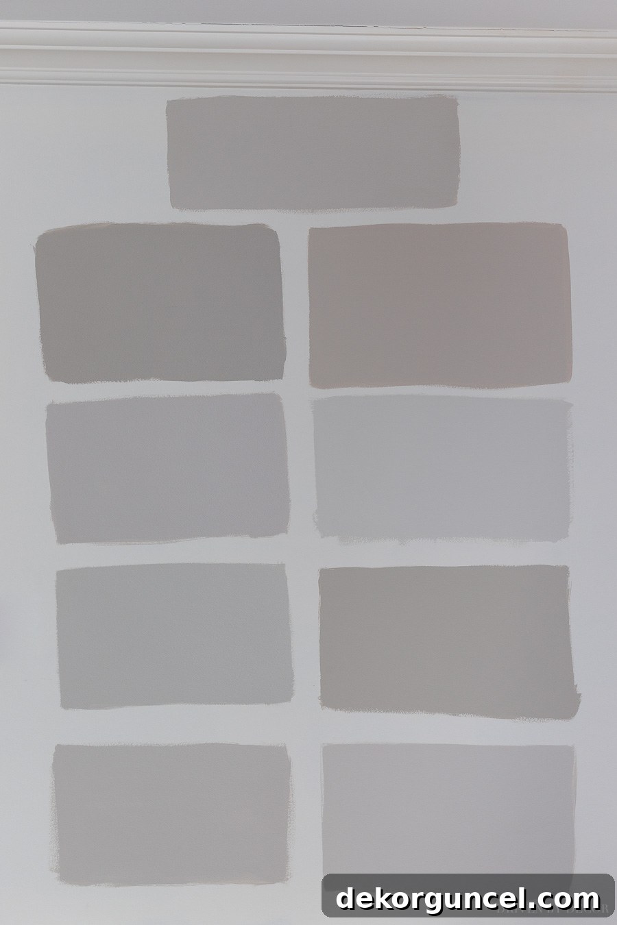 Nine of the top greige paint colors sampled on a wall for comparison, including Sherwin Williams Anew Gray, Alpaca, Repose Gray, Agreeable Gray, Worldly Gray; Behr Wheat Bread, Silver Drop; Benjamin Moore Revere Pewter, Balboa Mist.