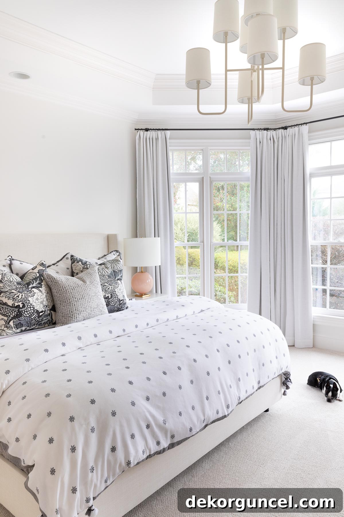Guest room bedding in shades of gray in bedroom with tall windows and chandelier