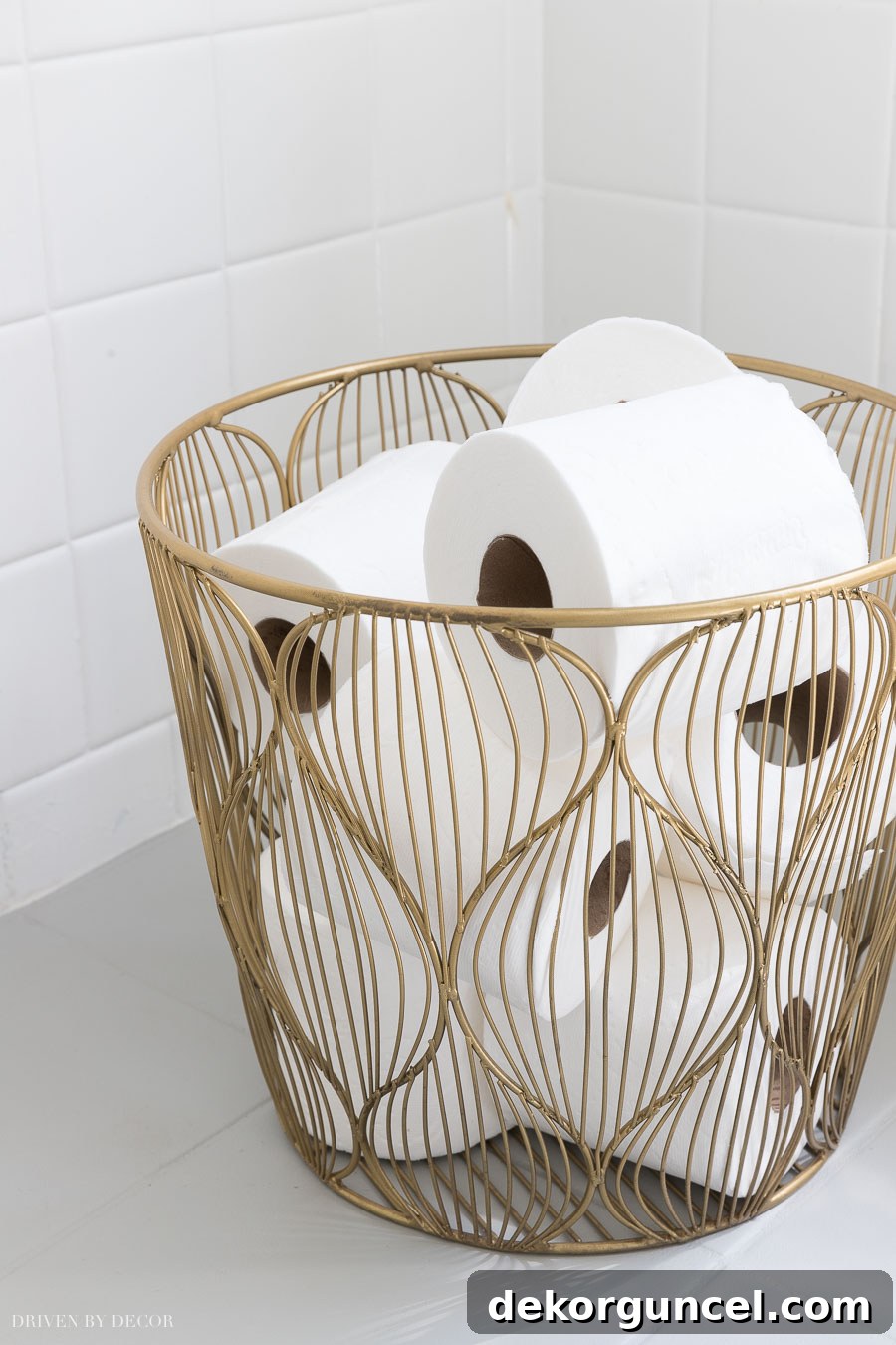 A small, elegant gold wire basket, perfectly sized to hold extra rolls of toilet paper, adding a touch of sophistication to the bathroom.