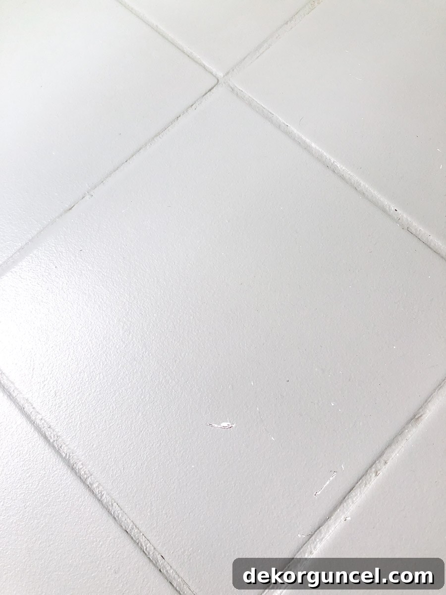 Close-up of painted tile floor showing minor scrapes and marks in front of the toilet after four years of use.