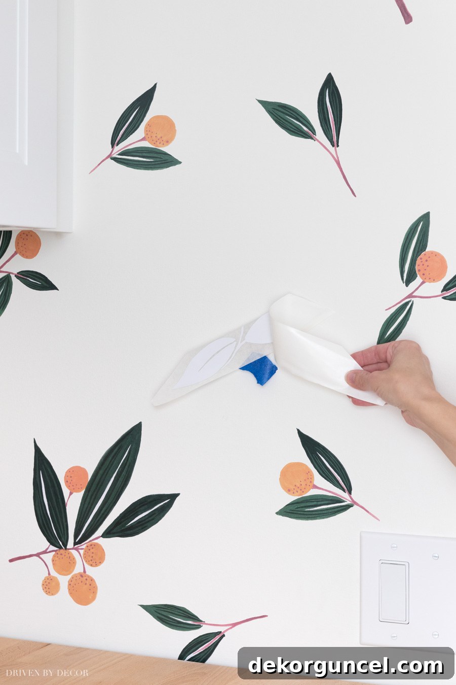The process of removing painter's tape and the rest of the backing paper from a vinyl wall decal, revealing the adhesive surface.