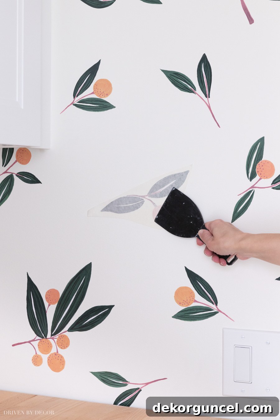 Using a flat-edged tool to firmly press and smooth a tangerine vinyl wall decal onto the wall, ensuring complete adhesion and removal of air bubbles.