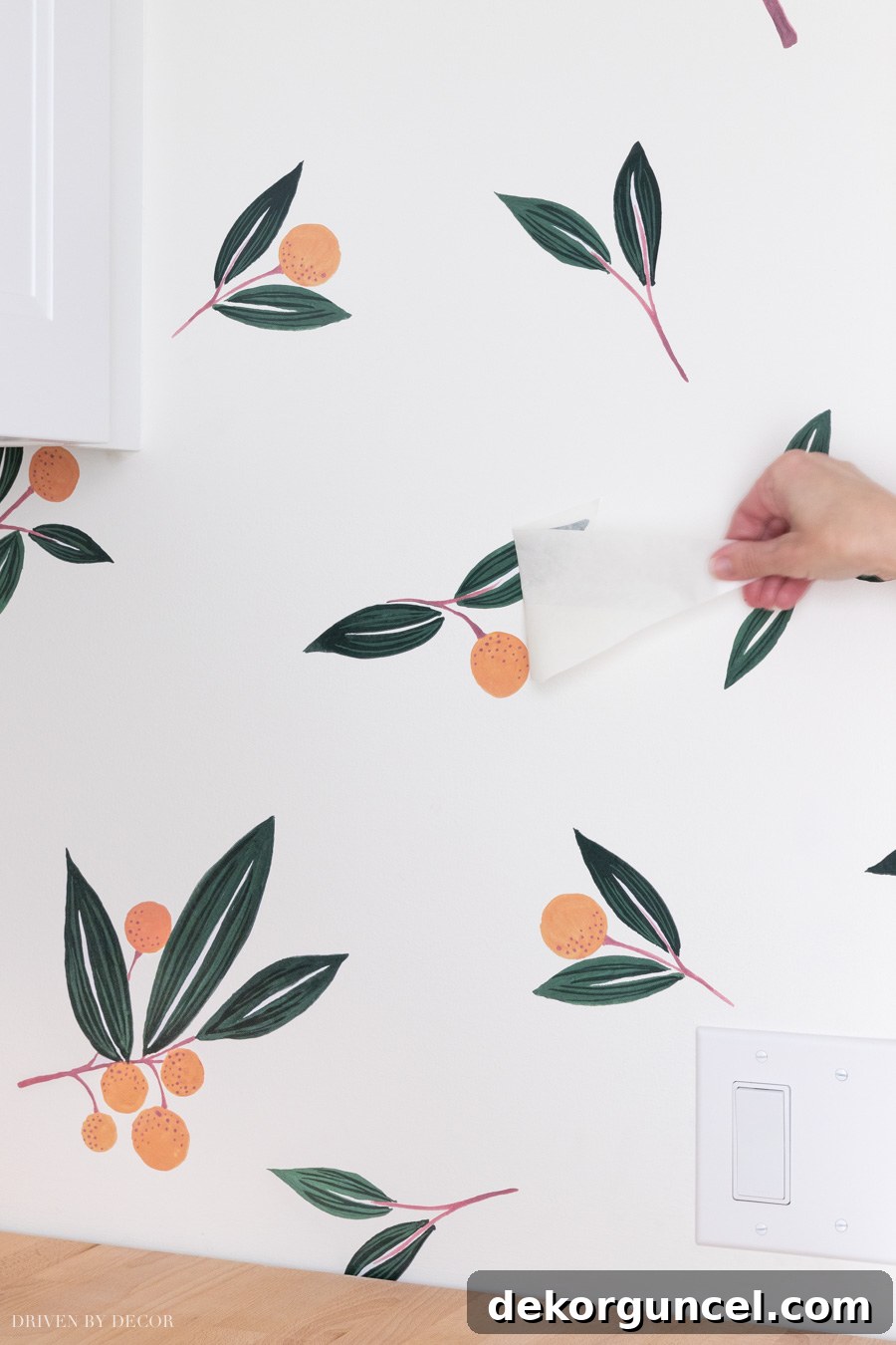 The final stage of application: gently peeling away the top transfer paper from a vinyl wall decal to reveal the vibrant design adhered to the wall.