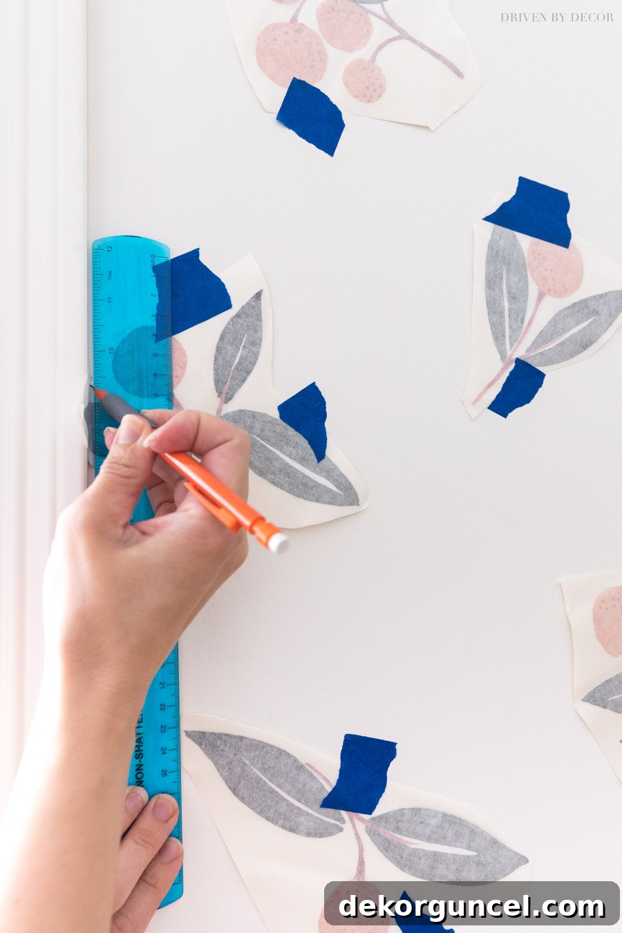 A close-up demonstration of how to use a ruler and pencil to accurately mark a cutting line for a vinyl wall decal that overlaps a wall's edge.