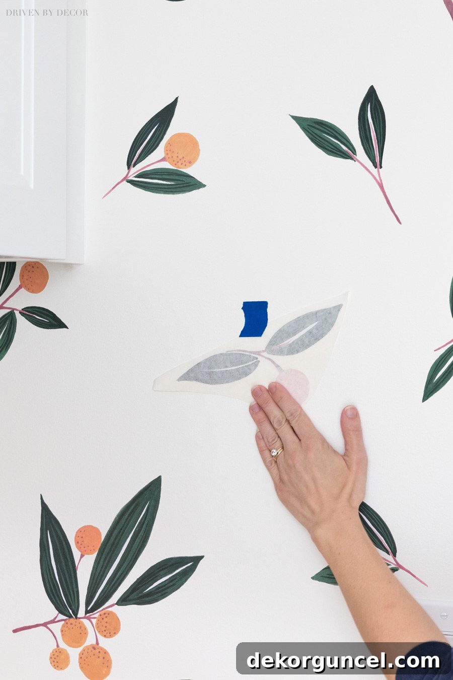 A hand gently smoothing the initial, partially-backed section of a vinyl wall decal onto the wall for a secure adhesion.