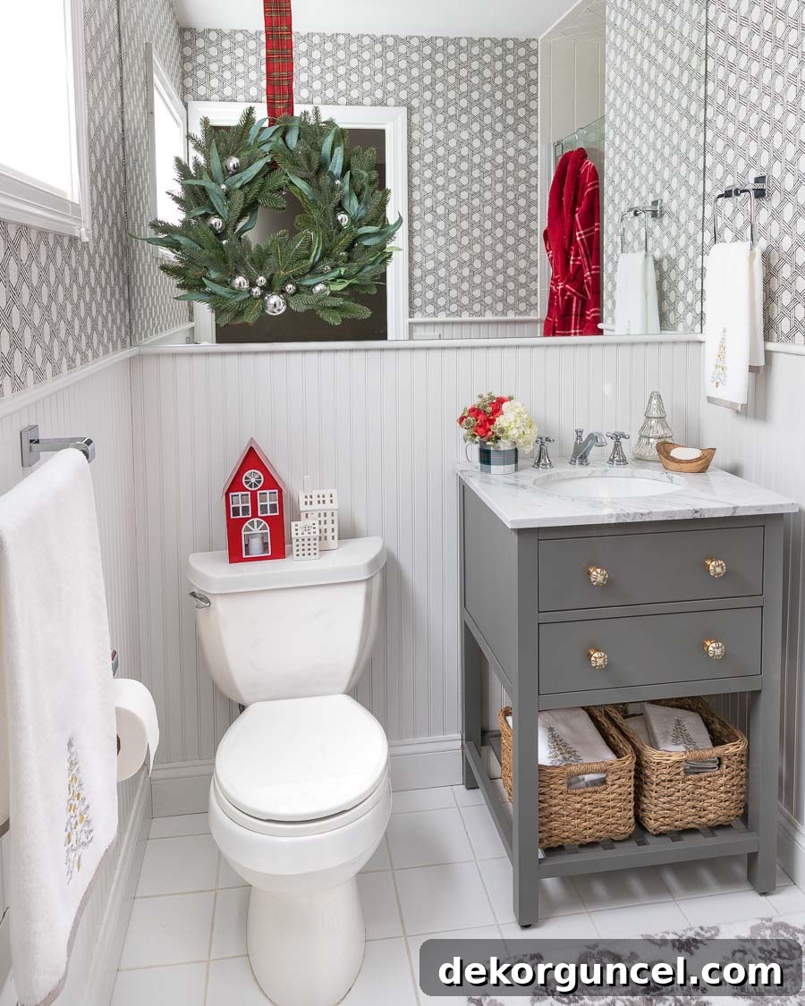 A charming guest bathroom adorned for Christmas with miniature LED houses, festive towels, and a wreath elegantly layered over the mirror.