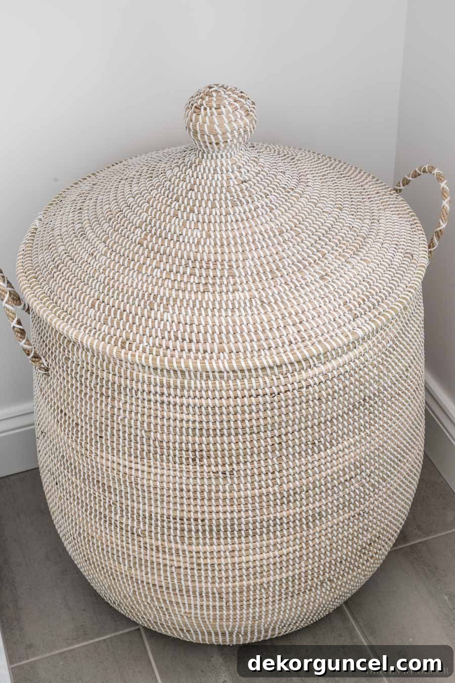 A large woven seagrass hamper with a lid, positioned below the floating shelves in our master bathroom