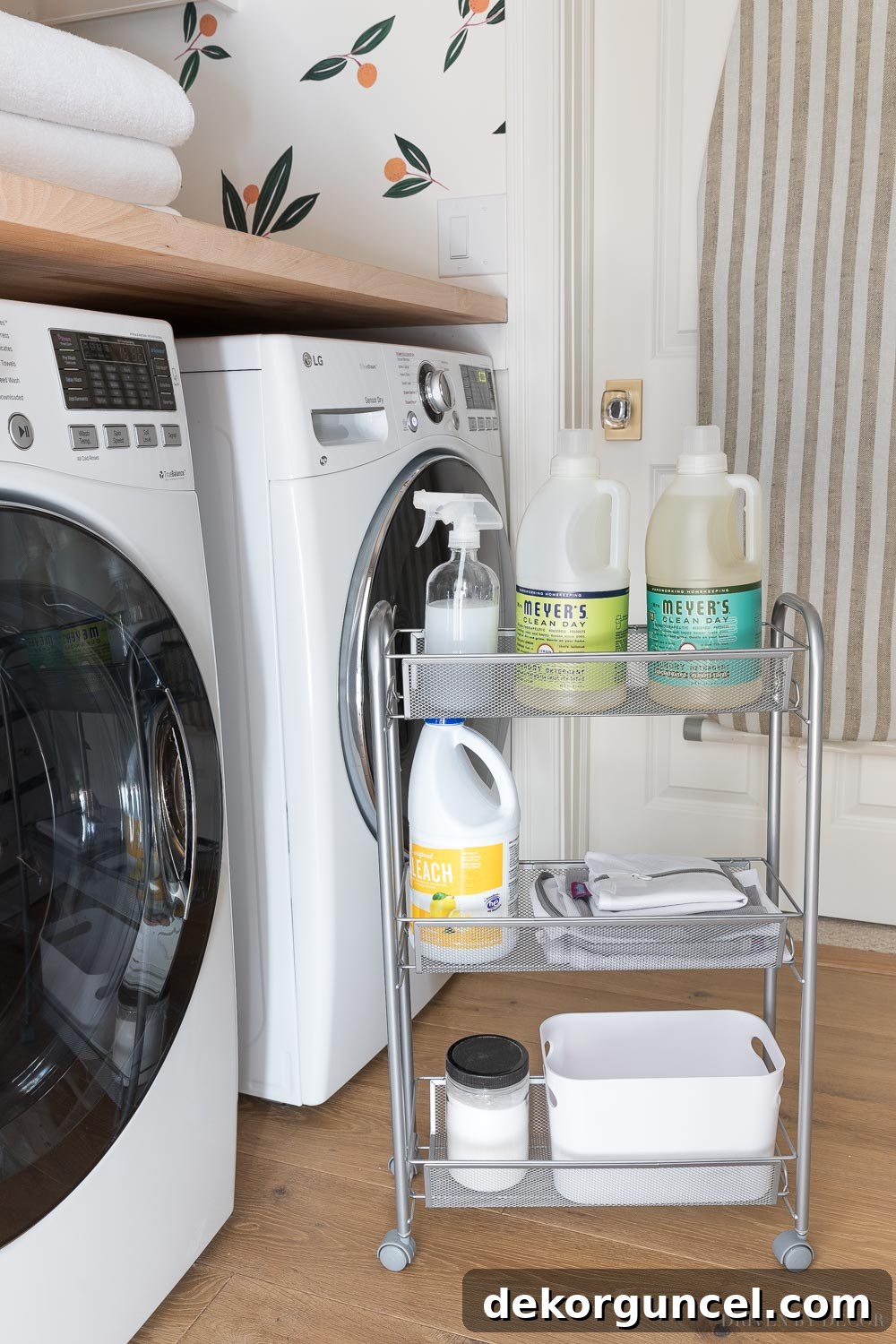 Close-up of a rolling cart between a washer and dryer, showing various laundry essentials organized in a bin, including detergent and delicates bags.