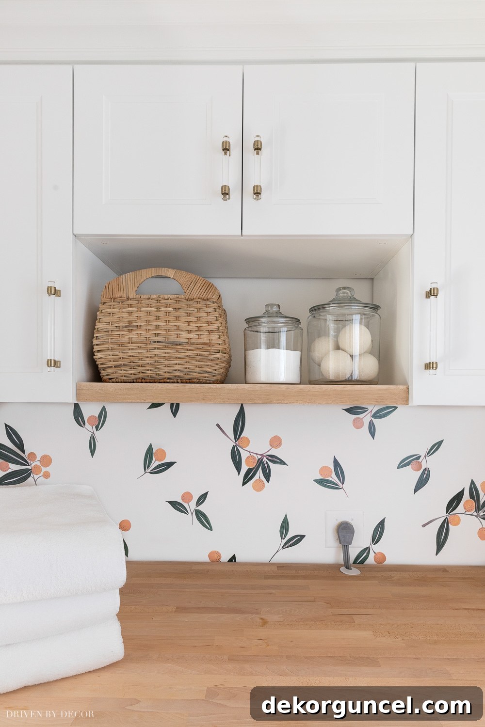 Open wood shelf positioned between IKEA cabinets in a laundry room, styled with a woven basket and glass jars for practical and decorative storage.