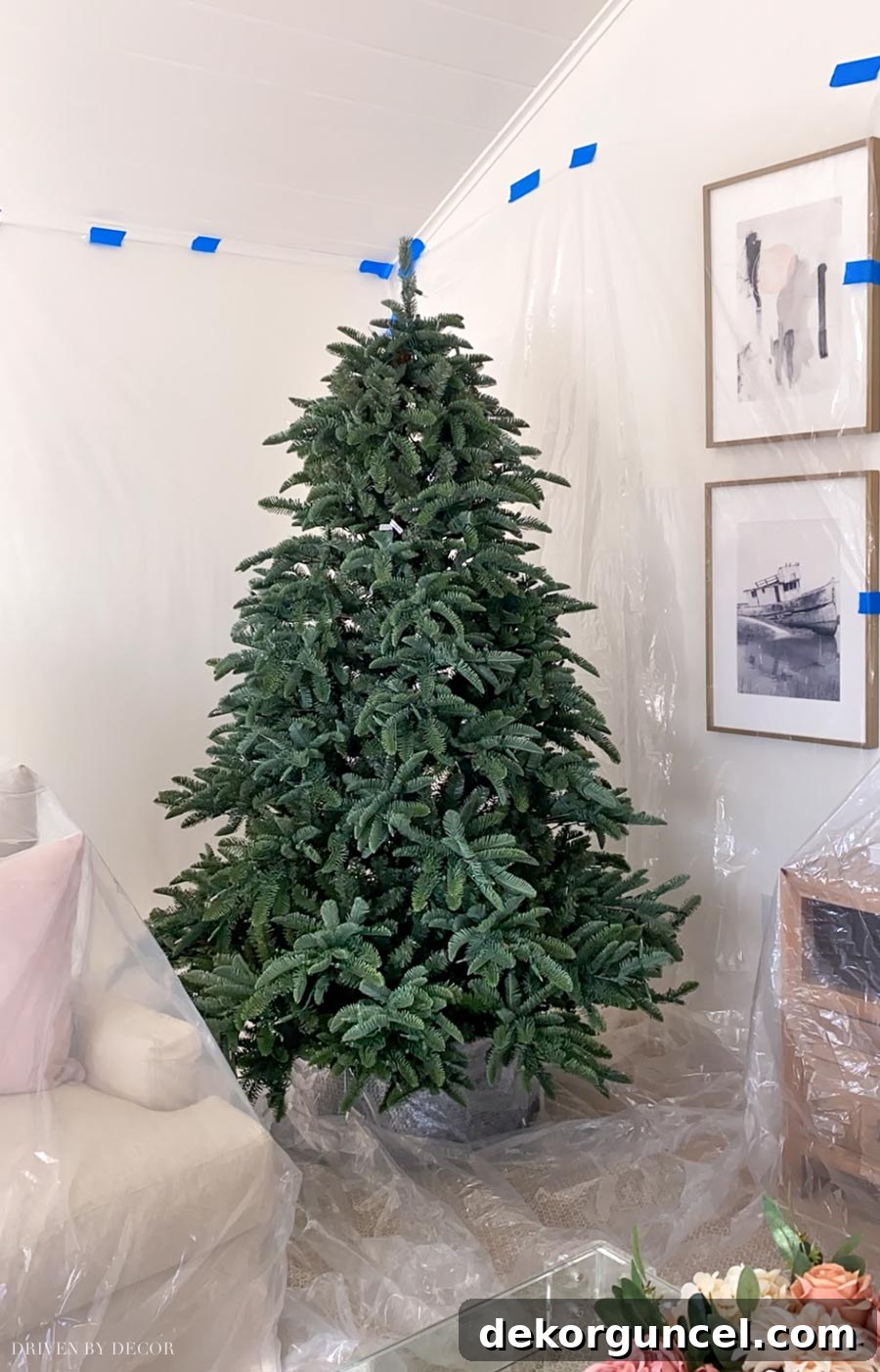 How to Perfectly Flock a Christmas Tree 4 A Christmas tree surrounded by meticulously taped plastic drop cloths, illustrating the essential protection needed when flocking your tree indoors to safeguard walls, floors, and furniture from stray flocking powder.