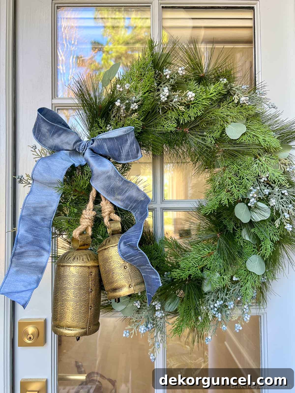 Greenery wreath decorated with a French blue ribbon and two bronze bells on a front door