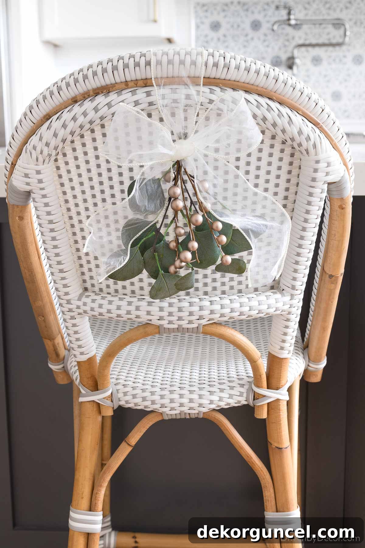 Chair backs decorated with sprigs of faux eucalyptus and gold berries tied with sheer white ribbon for simple Christmas decor