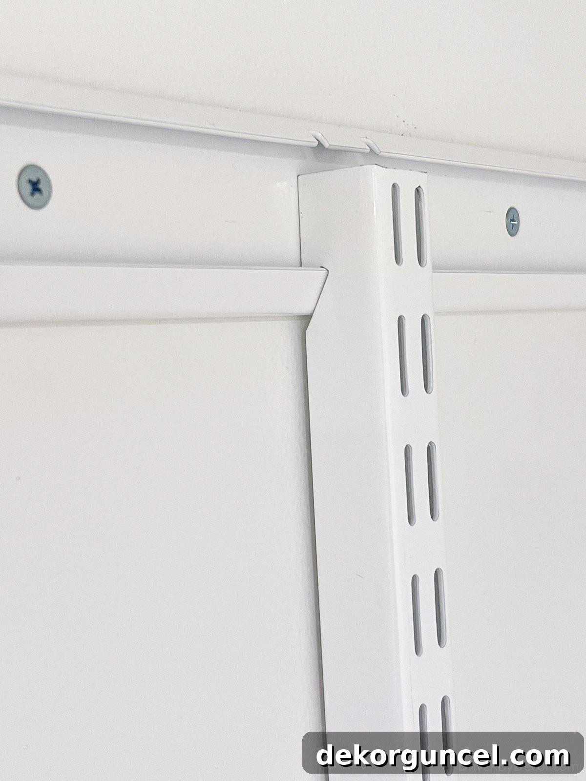 The vertical rails of the Elfa closet system being hooked onto the pre-installed top rail, forming the structural backbone.