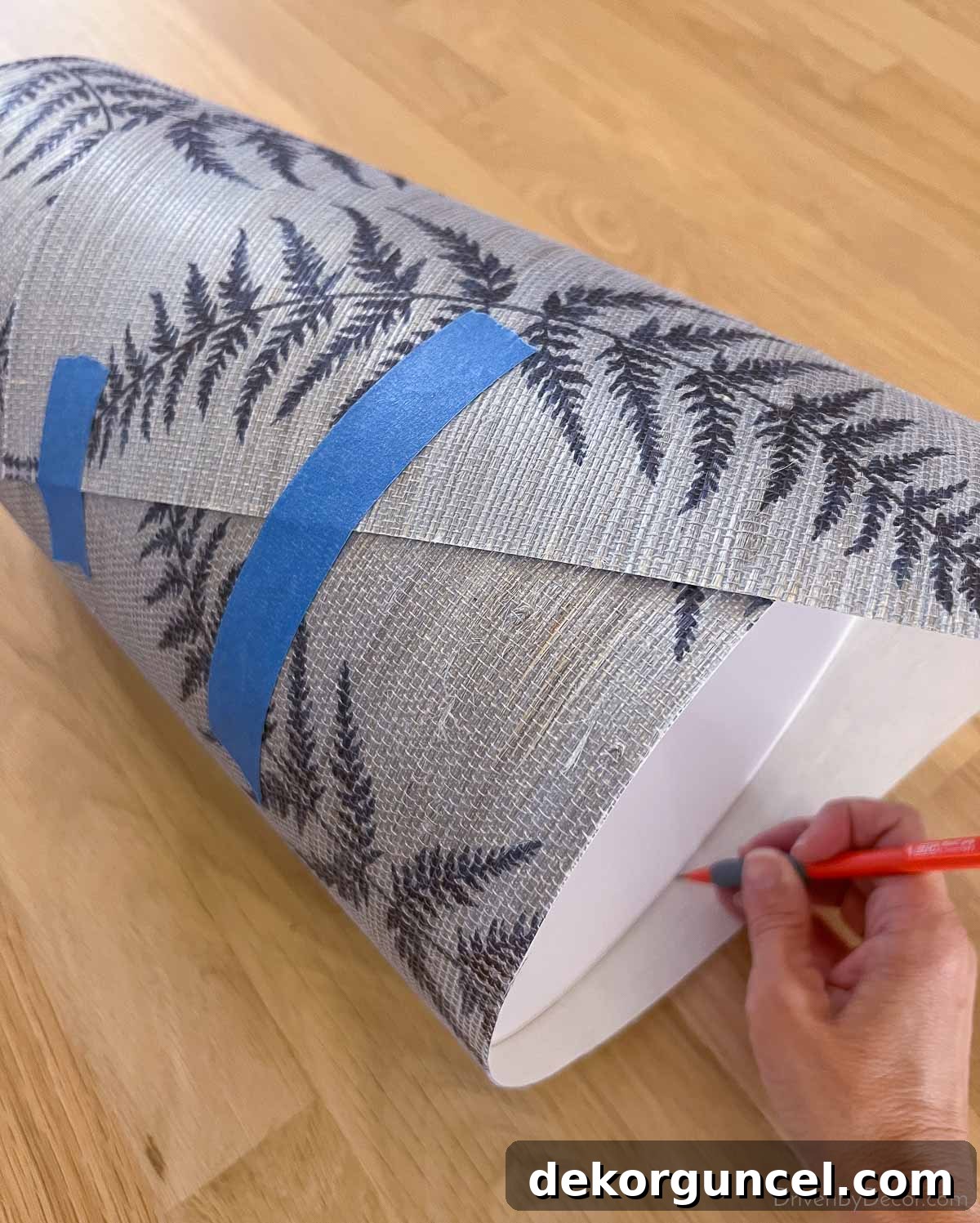 Grasscloth wallpaper remnant being wrapped around a waste basket, ready for precise cutting to size