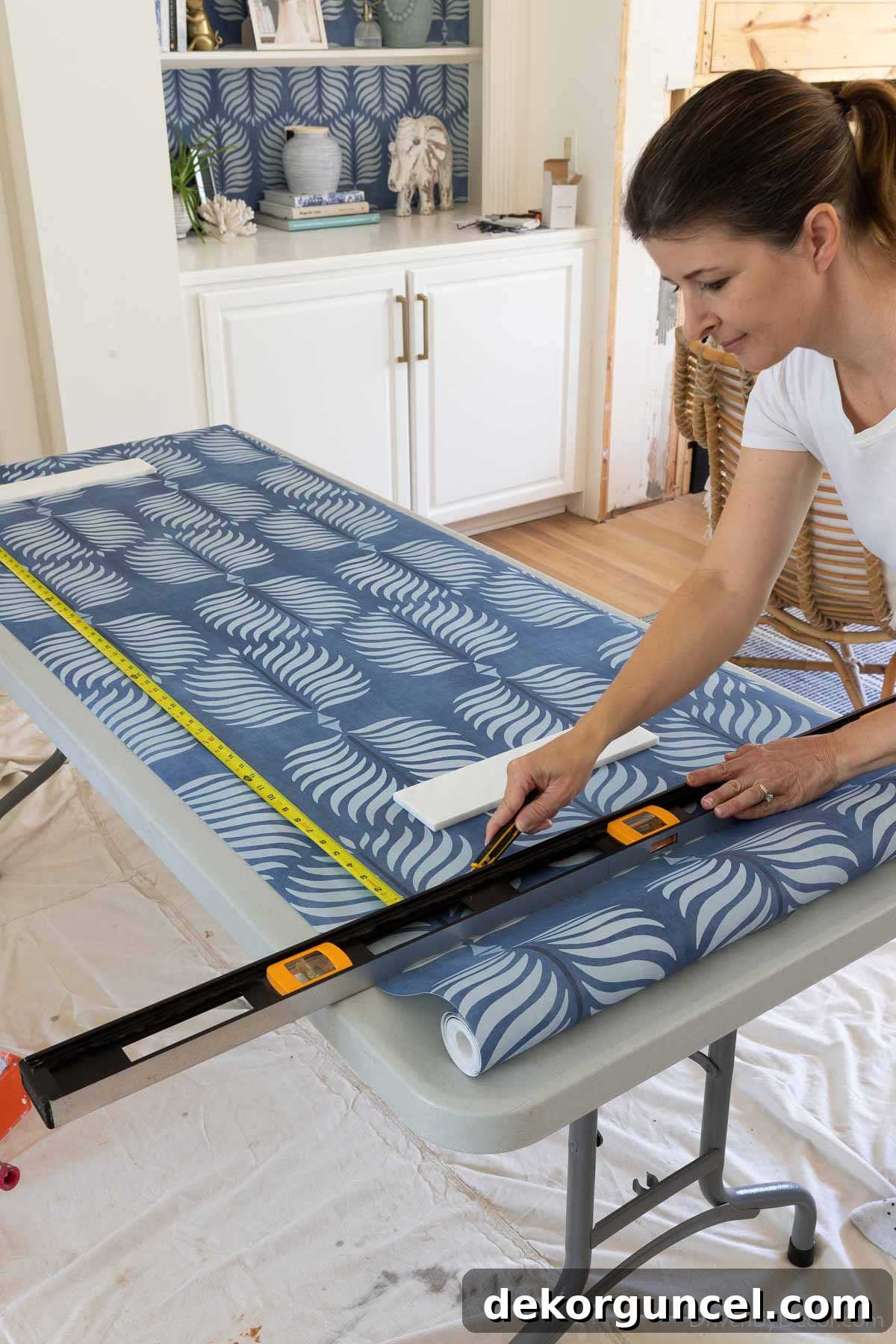 Measuring and cutting a wallpaper strip, ensuring extra length for trimming at the top and bottom of the wall.