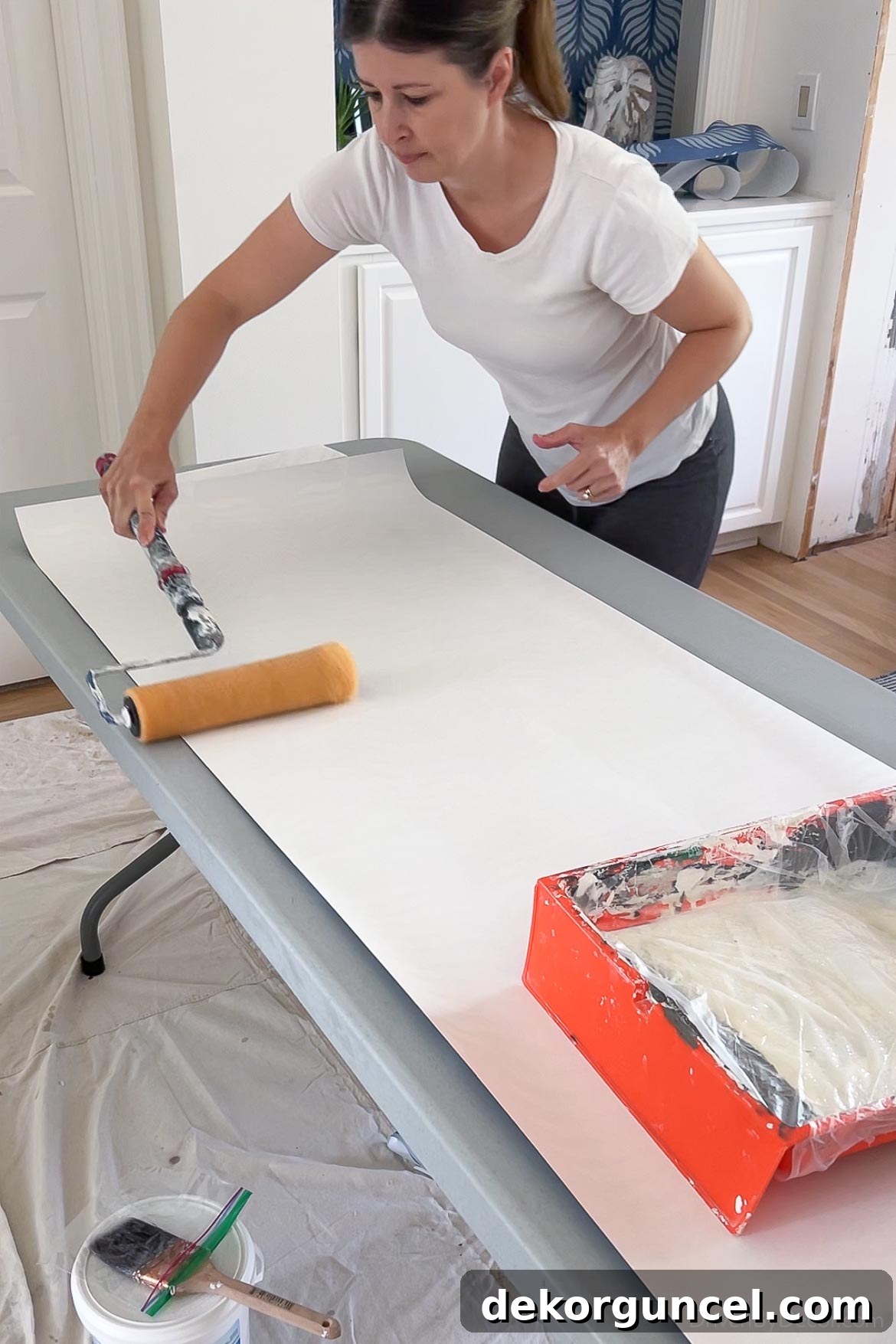 Applying wallpaper paste evenly to the back of a wallpaper strip with a roller, ensuring a thin and consistent coat.
