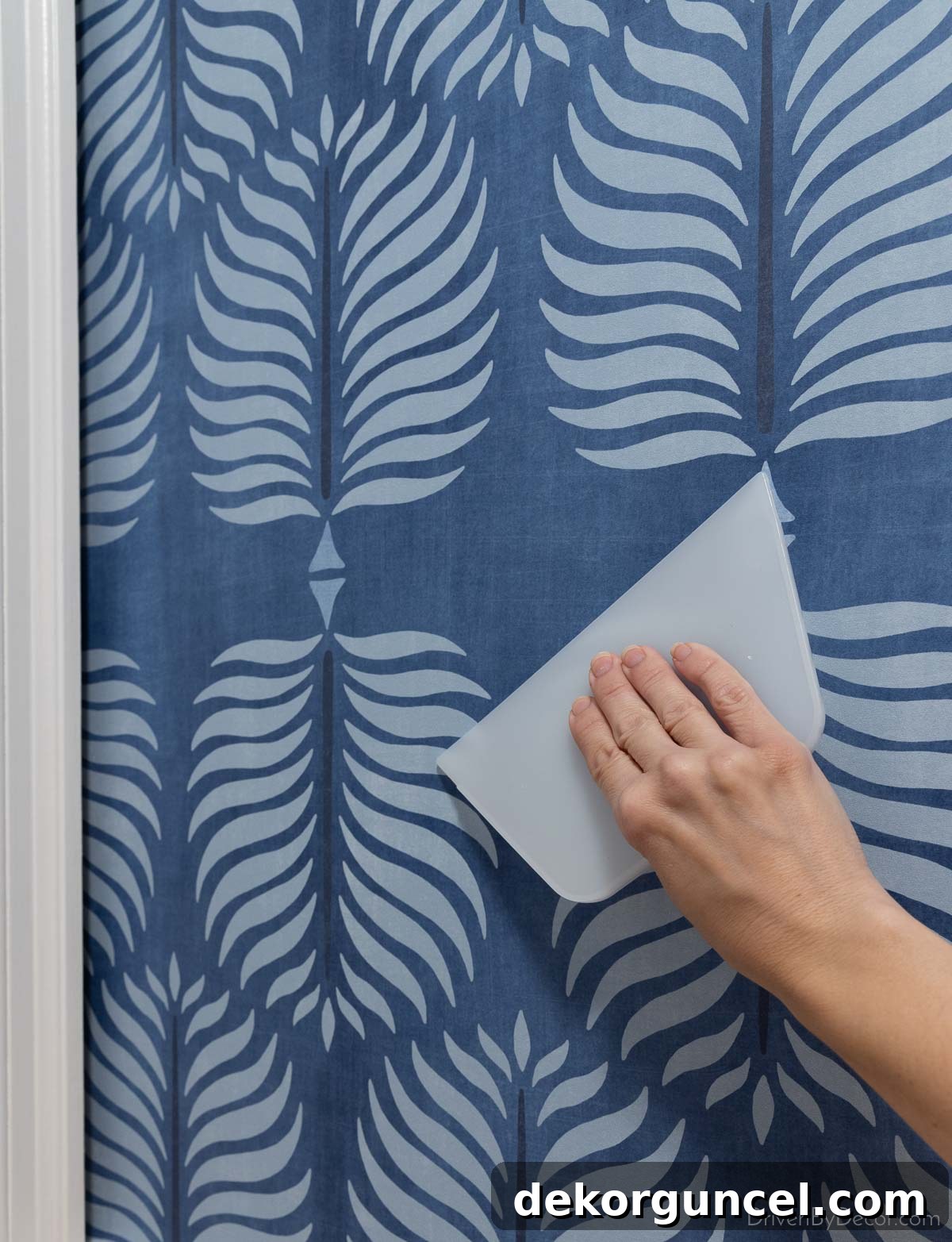 Using a wallpaper smoothing tool to gently press and remove air bubbles from a newly installed wallpaper strip, working from center to edge.
