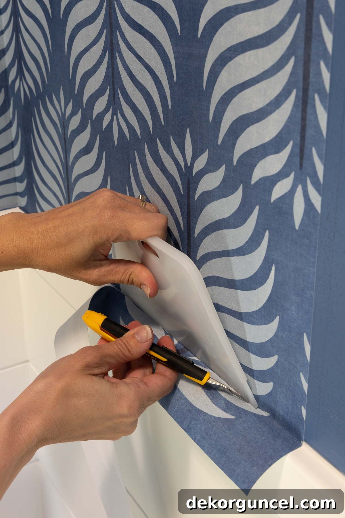 Demonstration of using a smoother as a straight edge with a sharp razor to precisely trim excess wallpaper at the bottom.