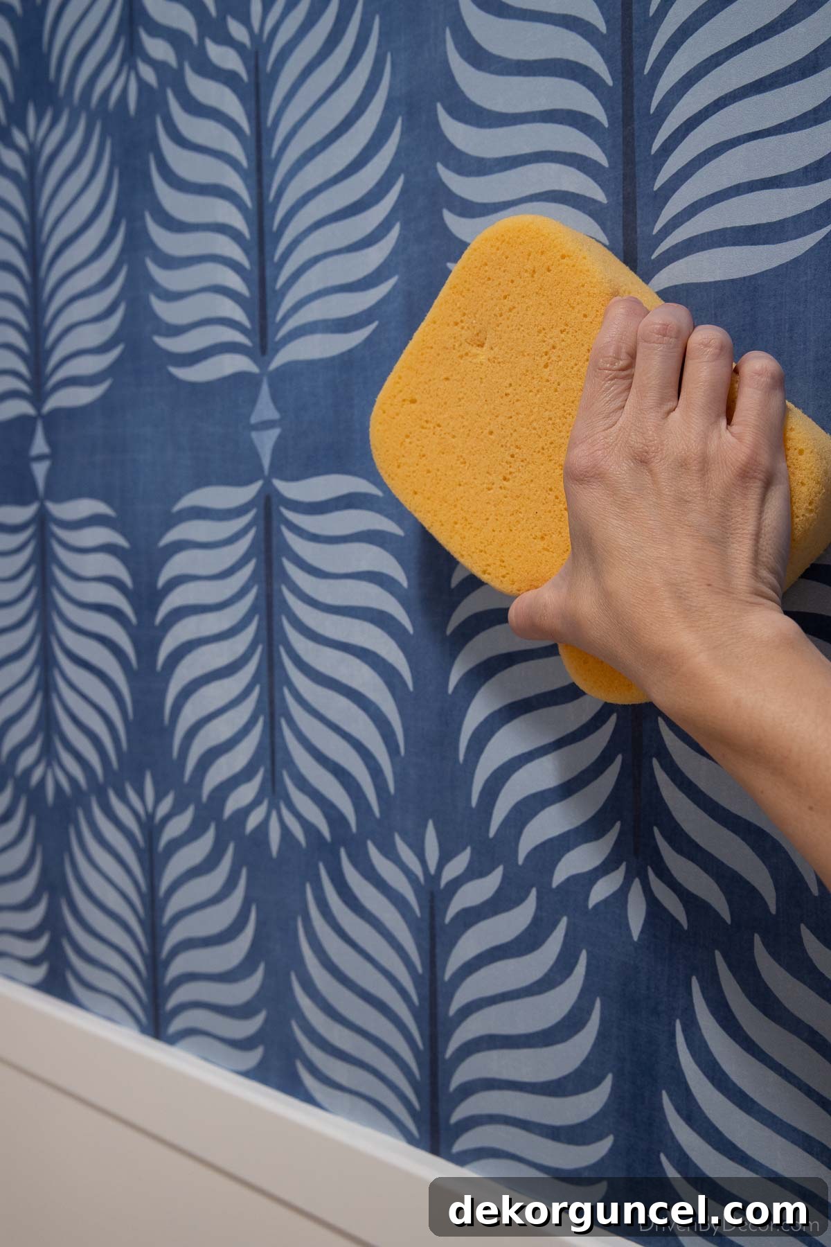 A hand using a damp sponge to carefully wipe off excess wallpaper glue from a newly installed panel, emphasizing immediate cleanup.