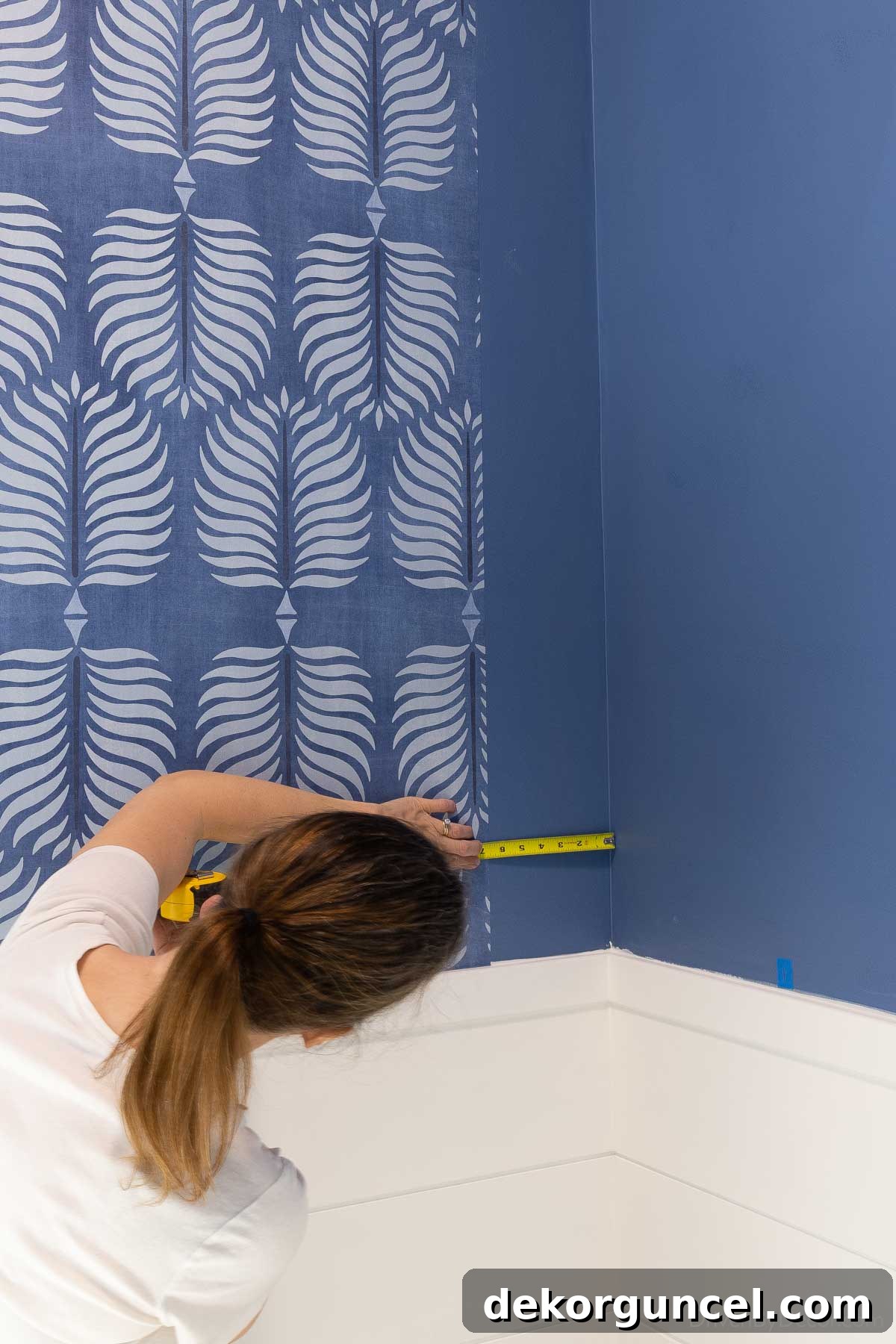 Measuring from the last wallpaper strip into a corner at multiple points to determine precise cut for corner installation.