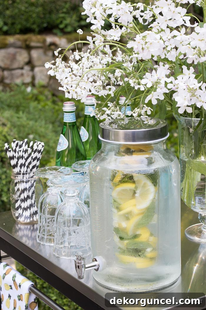 A stylish glass drink dispenser with an infuser filled with fruit, perfectly set up on an outdoor bar cart for summer entertaining.