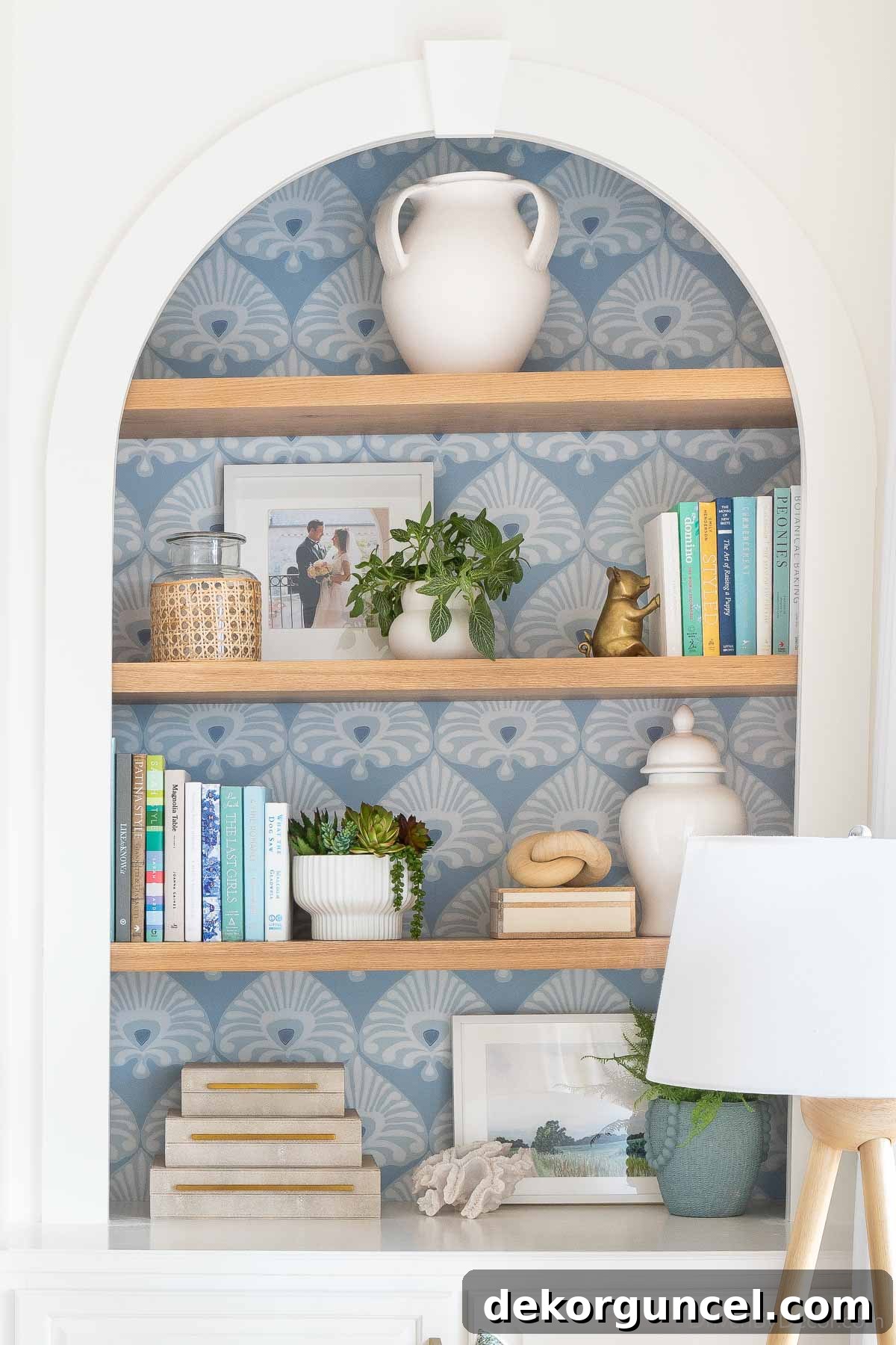 Blue patterned wallpaper on the back of a bookcase, featuring a stylish 3-handled vase