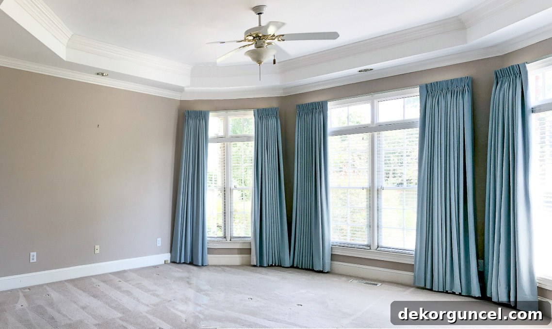 Primary bedroom before remodeling with beige walls, green curtains, and a ceiling fan