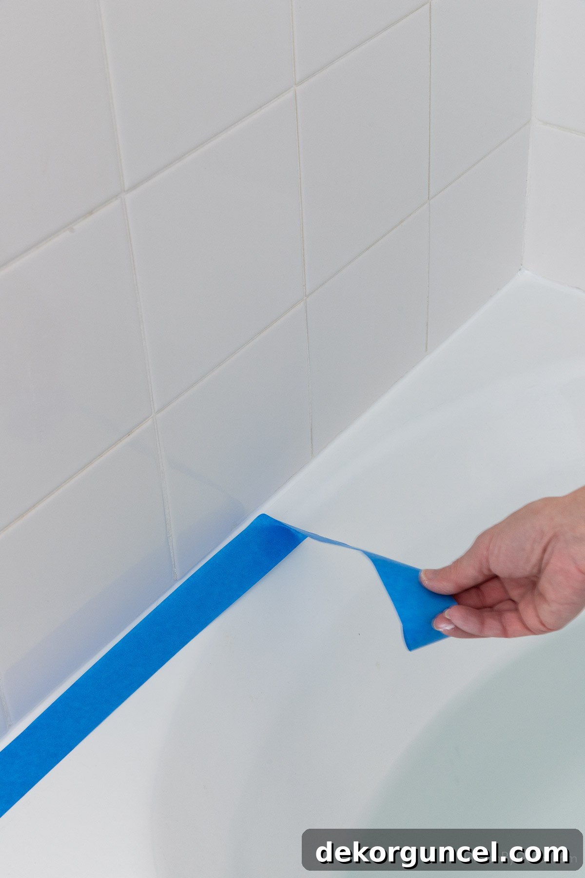 Removing painter's tape along a newly caulked bathtub joint, revealing a clean line
