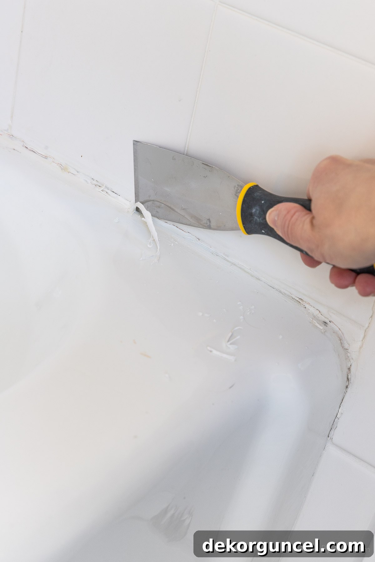 Using a putty knife to scrape the top edge of old caulk off of a bathtub