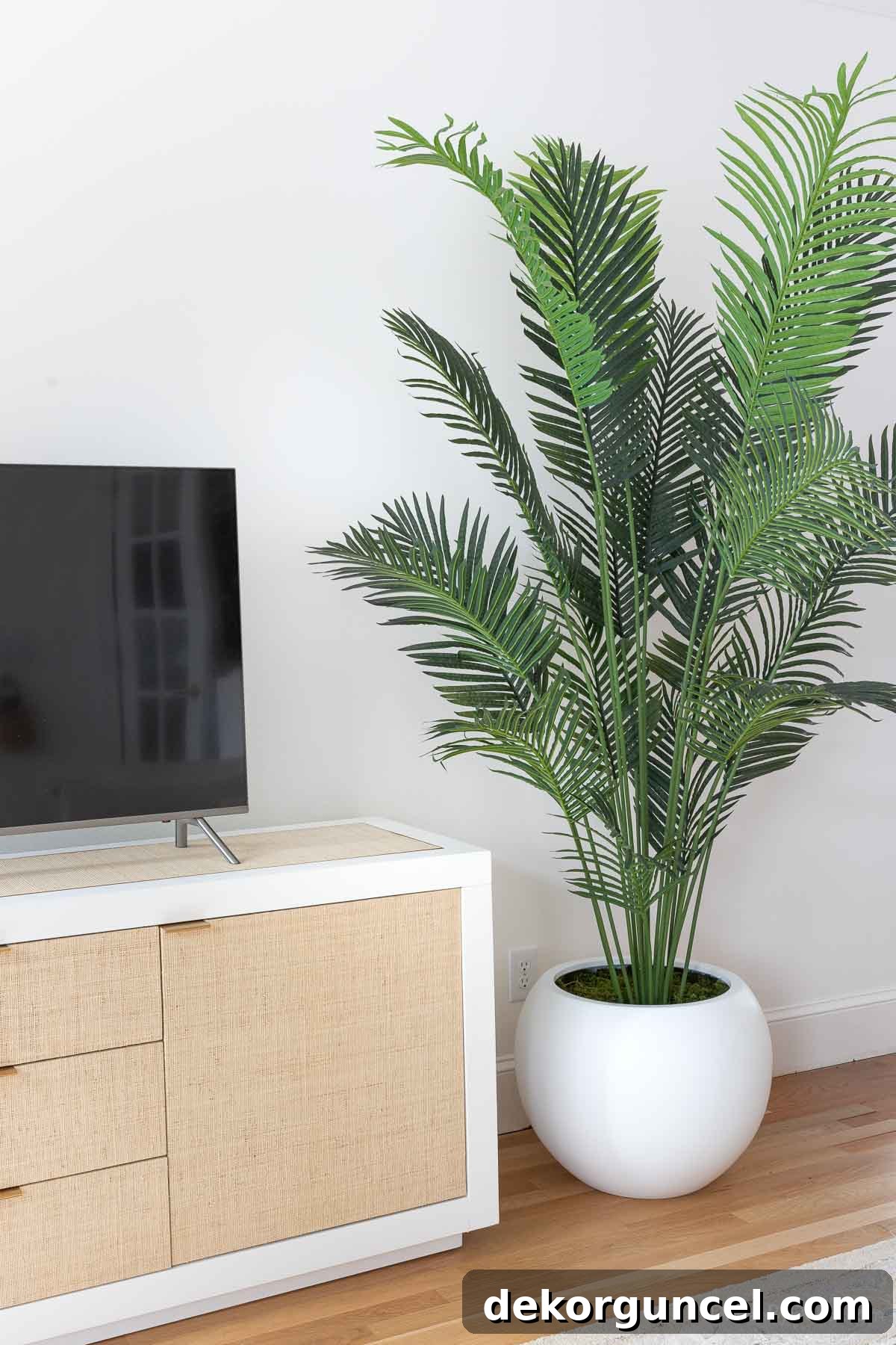 Large round white planter featuring a realistic faux palm tree next to a modern TV console