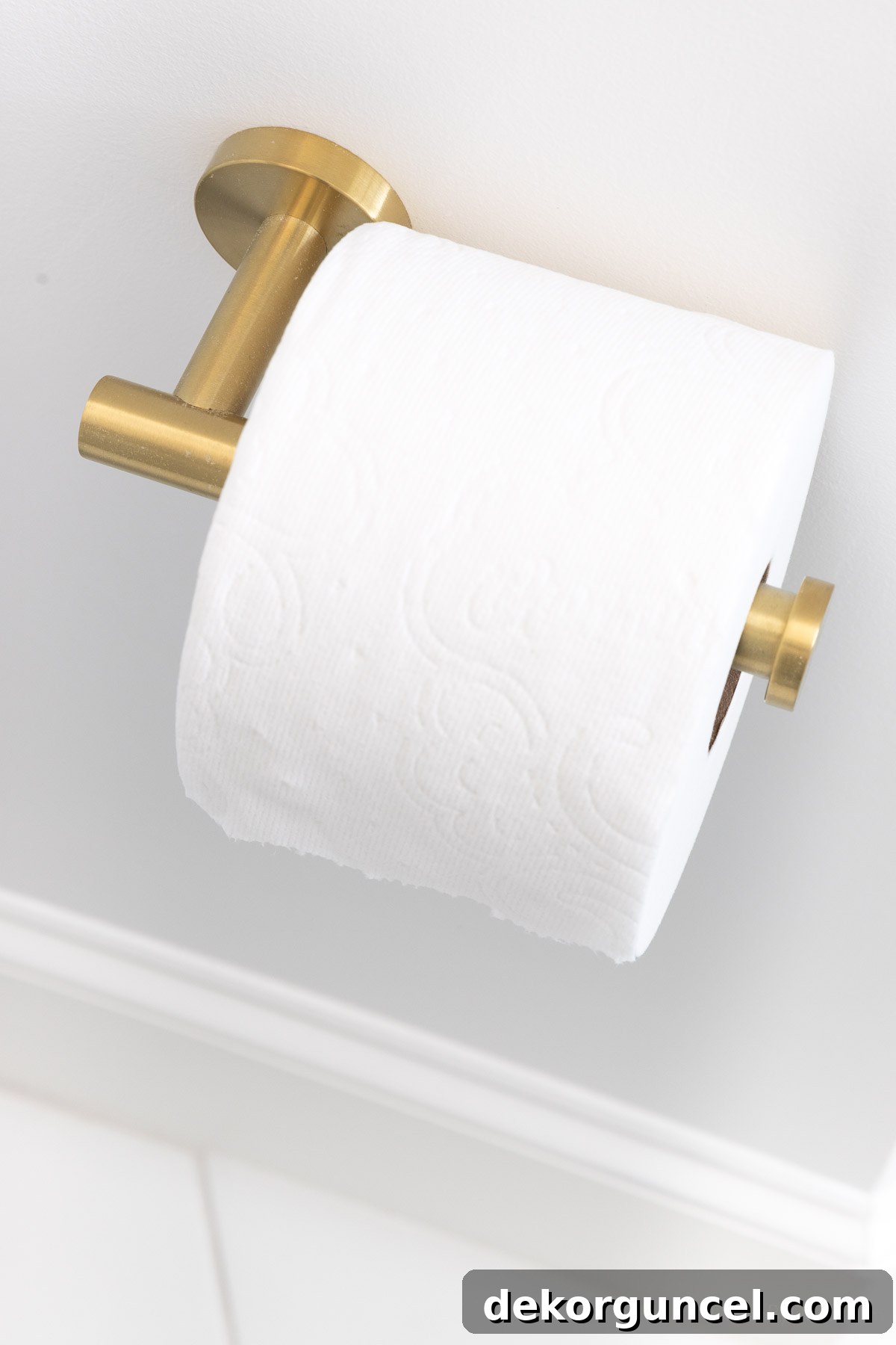 Simple brushed gold toilet paper holder mounted on the bathroom wall, complementing other brass fixtures