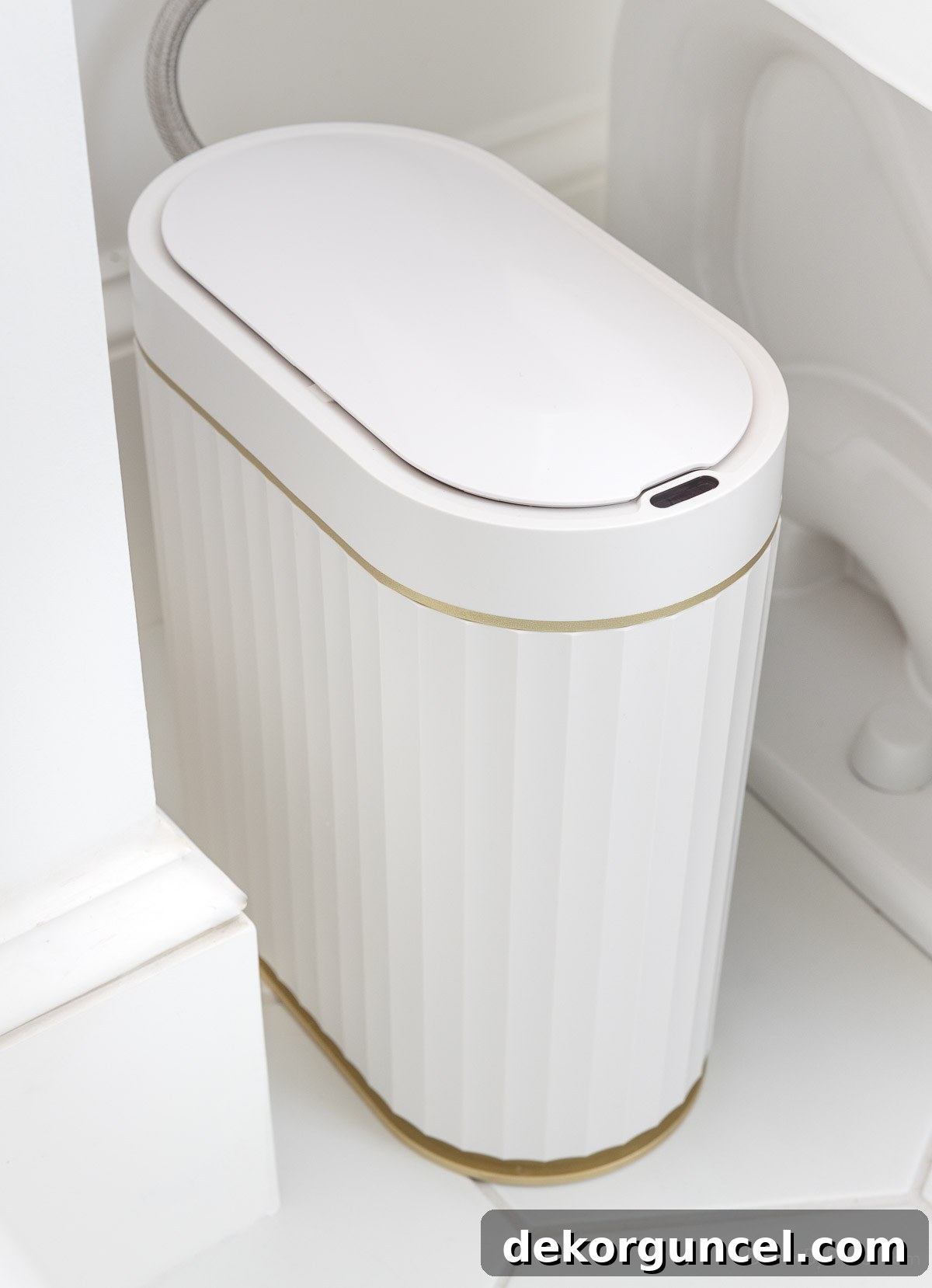 Slim ribbed motion-sensing trash can placed discreetly next to the toilet, featuring a modern design