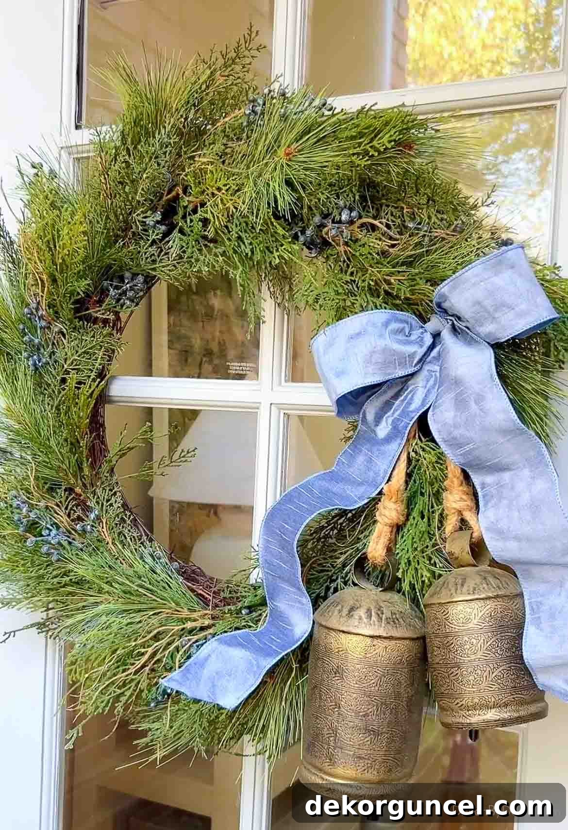 Festive juniper wreath adorned with blue ribbon and a pair of brass bells on a front door