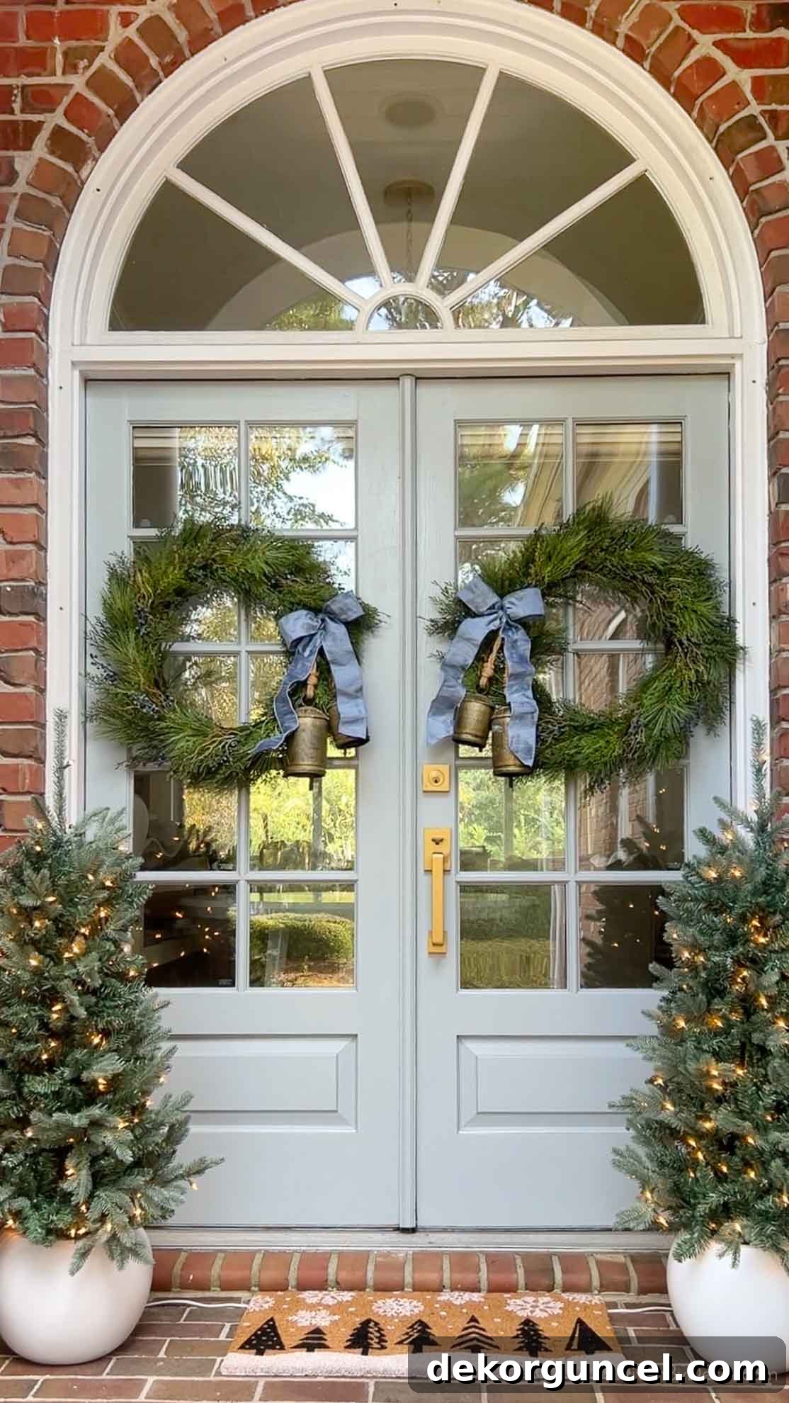 A beautifully decorated front porch for the holidays with wreaths, lighted trees, and a festive doormat